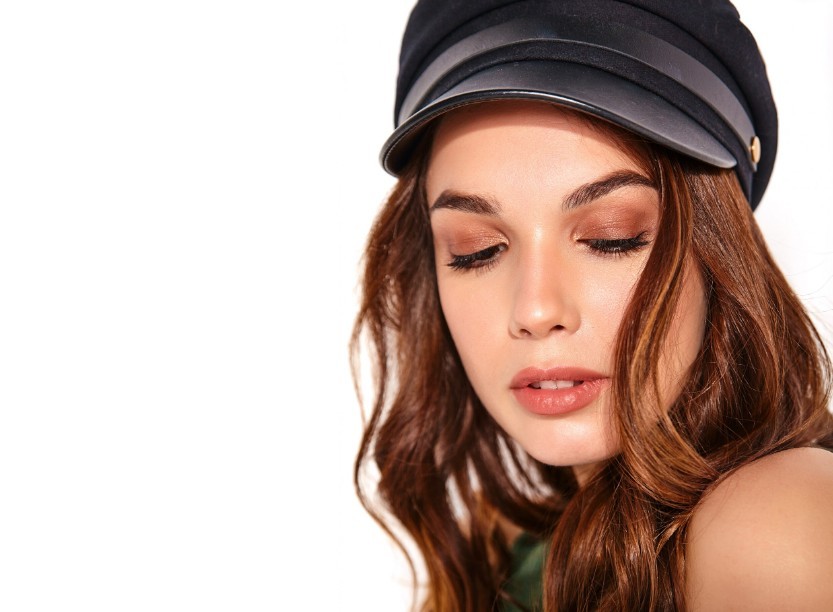 Model posing with bronze-brown eye shadow and a trendy hat