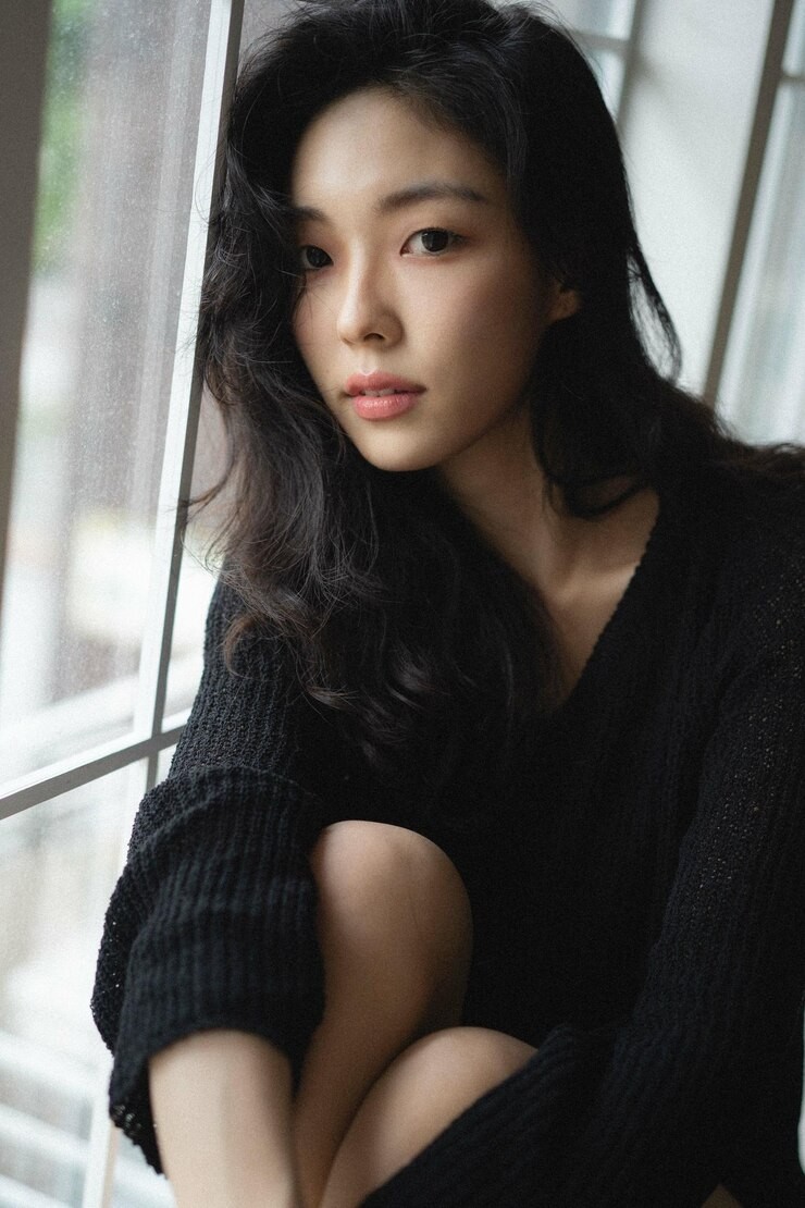Young woman sitting in front of camera in soft, black sweater and soft lighting