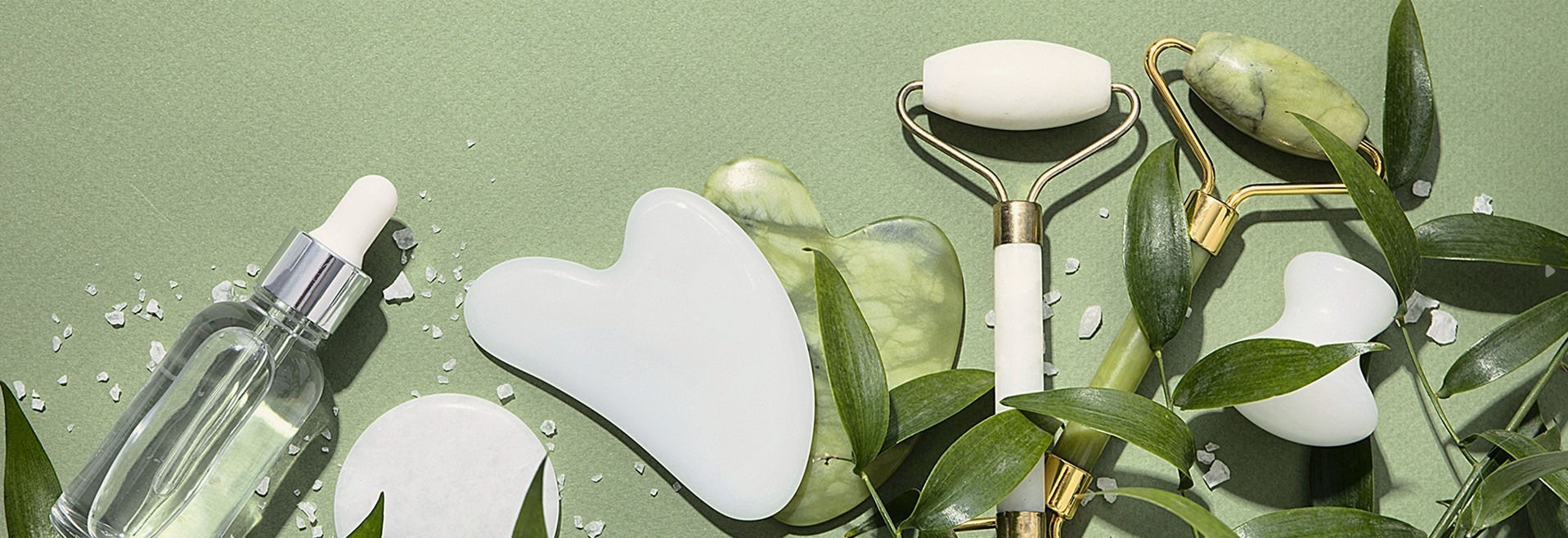 Gua Sha skincare arrangement with serum, oils and a floral branch