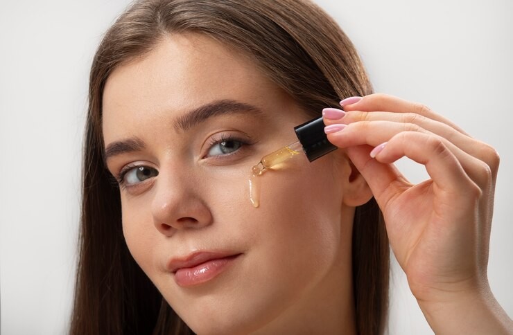 Young woman holding serum applicator to cheek, with golden serum dripping