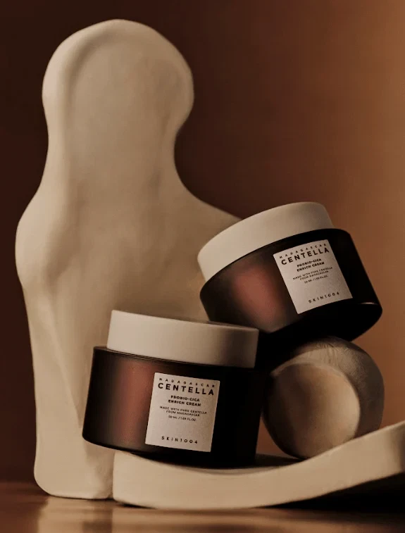 Pair of Skin1004 Madagascar Centella Probio-Cica Cream sitting on marble sculpture in low lighting