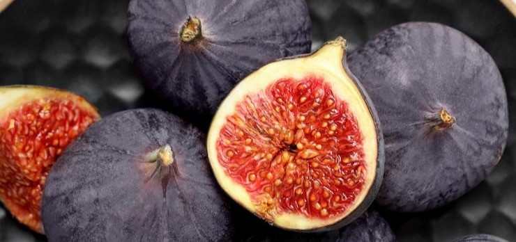 Cut section of a perfectly ripe, crimson fig balanced on other fresh figs