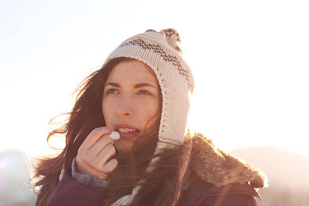 Woman with dark hair and beanie applying lip balm in cold weather