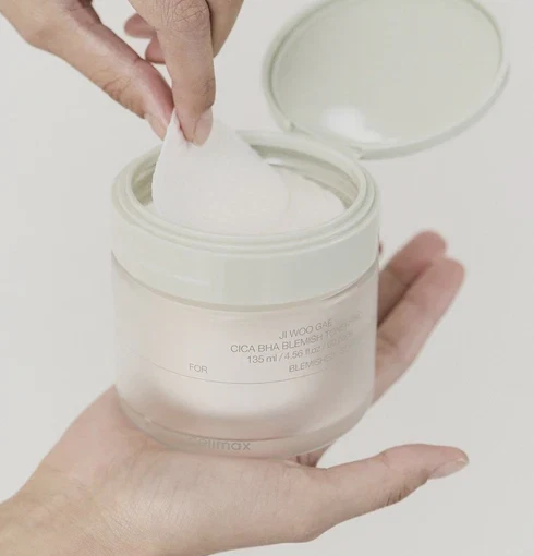 Model holding and lifting out a pad from the Celimax Ji Woo Gae Cica BHA Blemish Toner Container