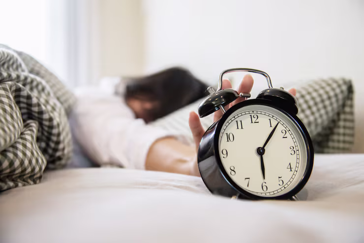 Sleeping person reaching for a ringing alarm clock in bed