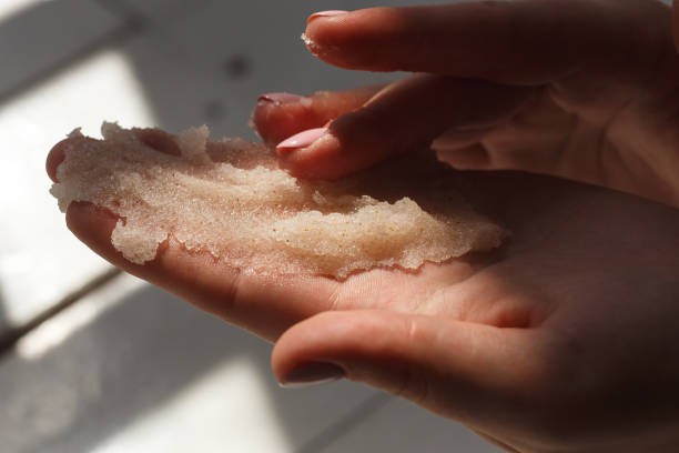 Hands holding exfoliating scrub between fingertips in low light