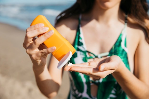 Young woman at the beach, applying sunscreen to her palm