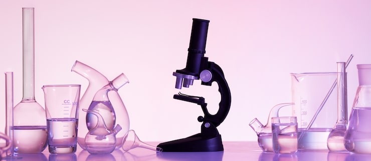 Microscope in low pink lighting surrounded by beakers, conical flasks and boiler flasks.