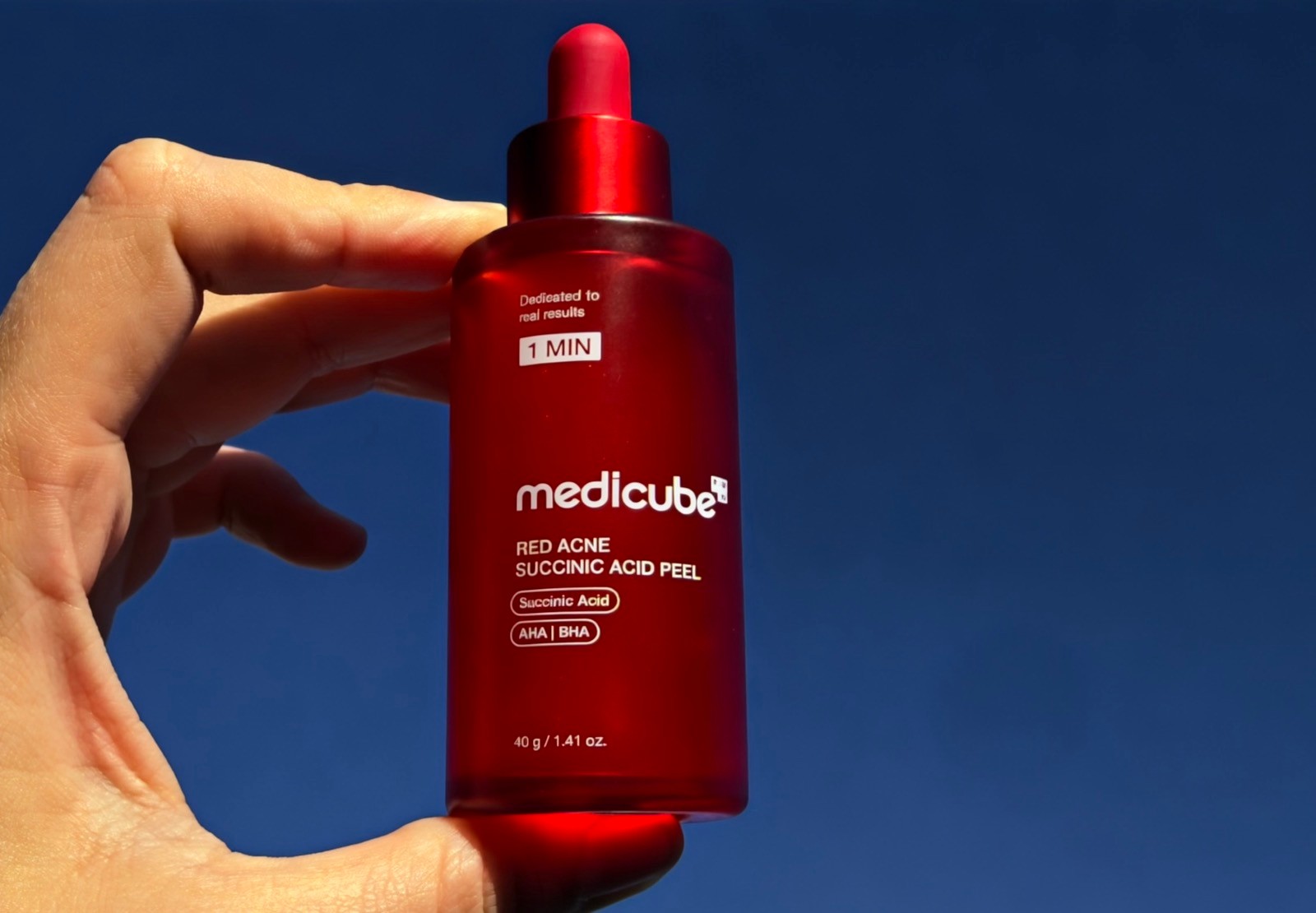 Person holding Medicube Red Acne Succinic Acid Peel AHA BHA skincare bottle outdoors