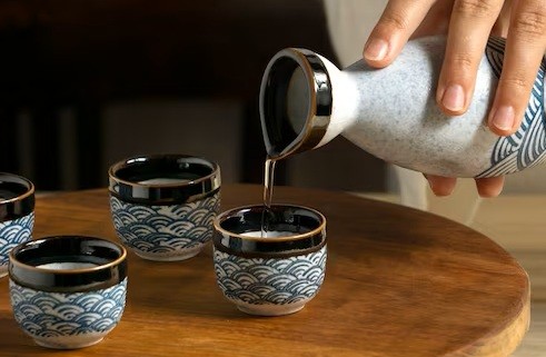 Steady hand pouring a warm cup of traditional sake