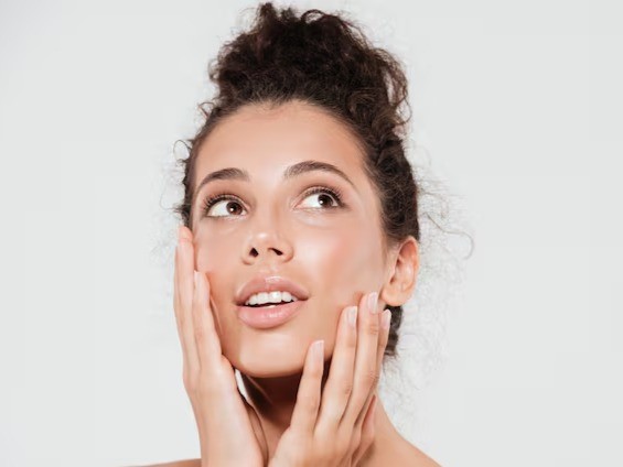 Young model with updo holding her face and looking upwards with shining skin