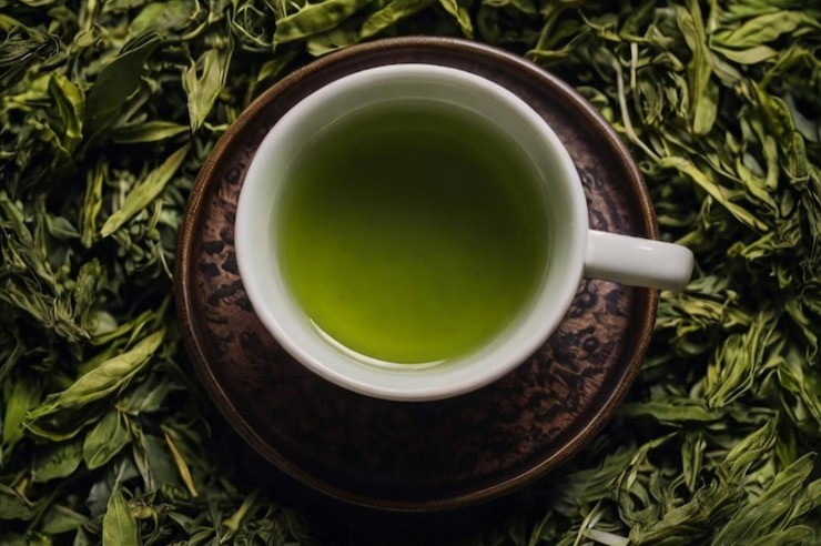 Cup of green tea lying on a bed of dried green tea leaves