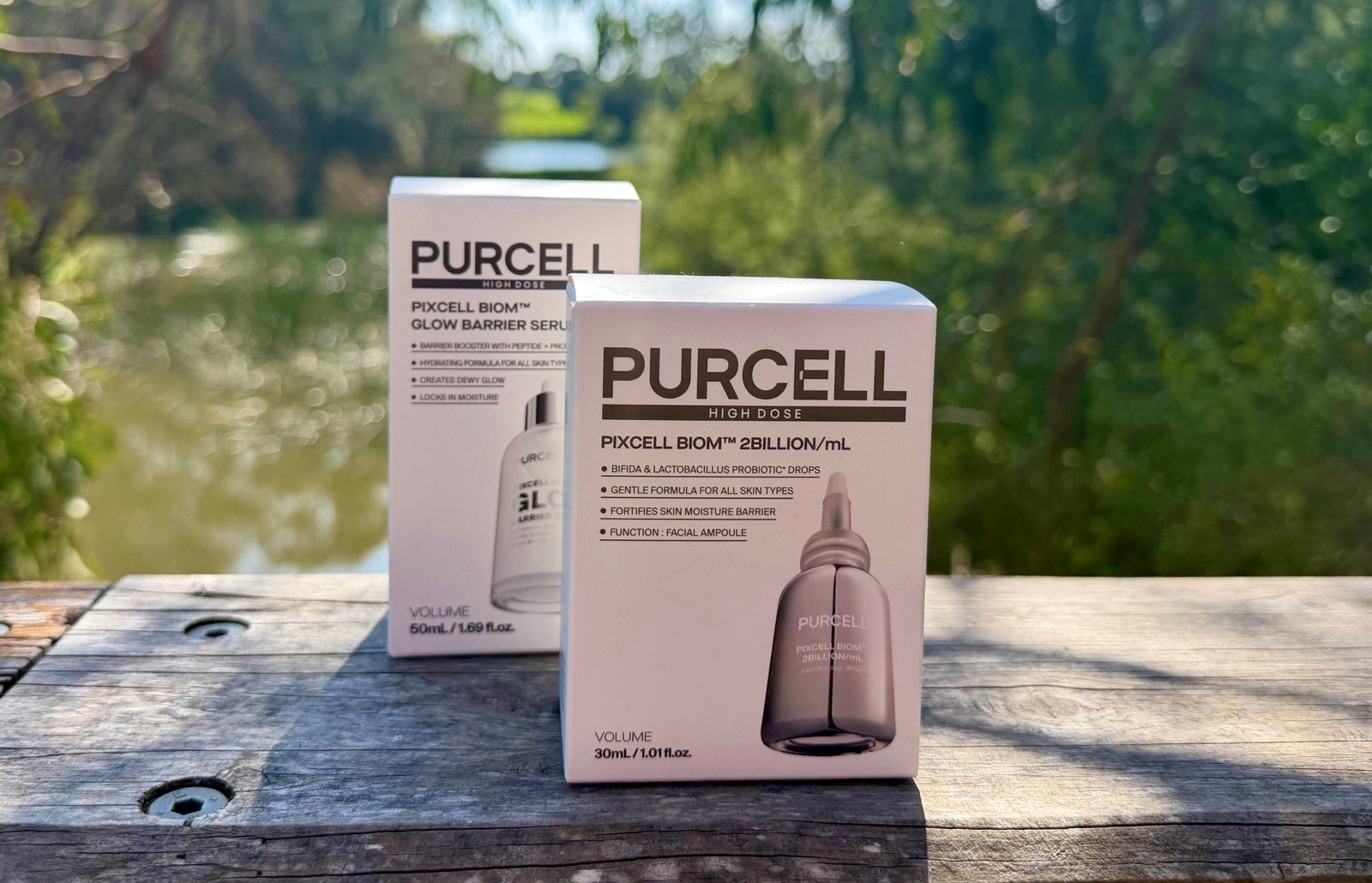 PURCELL High Dose Pixcell Biom 2Billion mL Facial Ampoule and Glow Barrier Serum boxes sitting on a wooden ledge outdoors