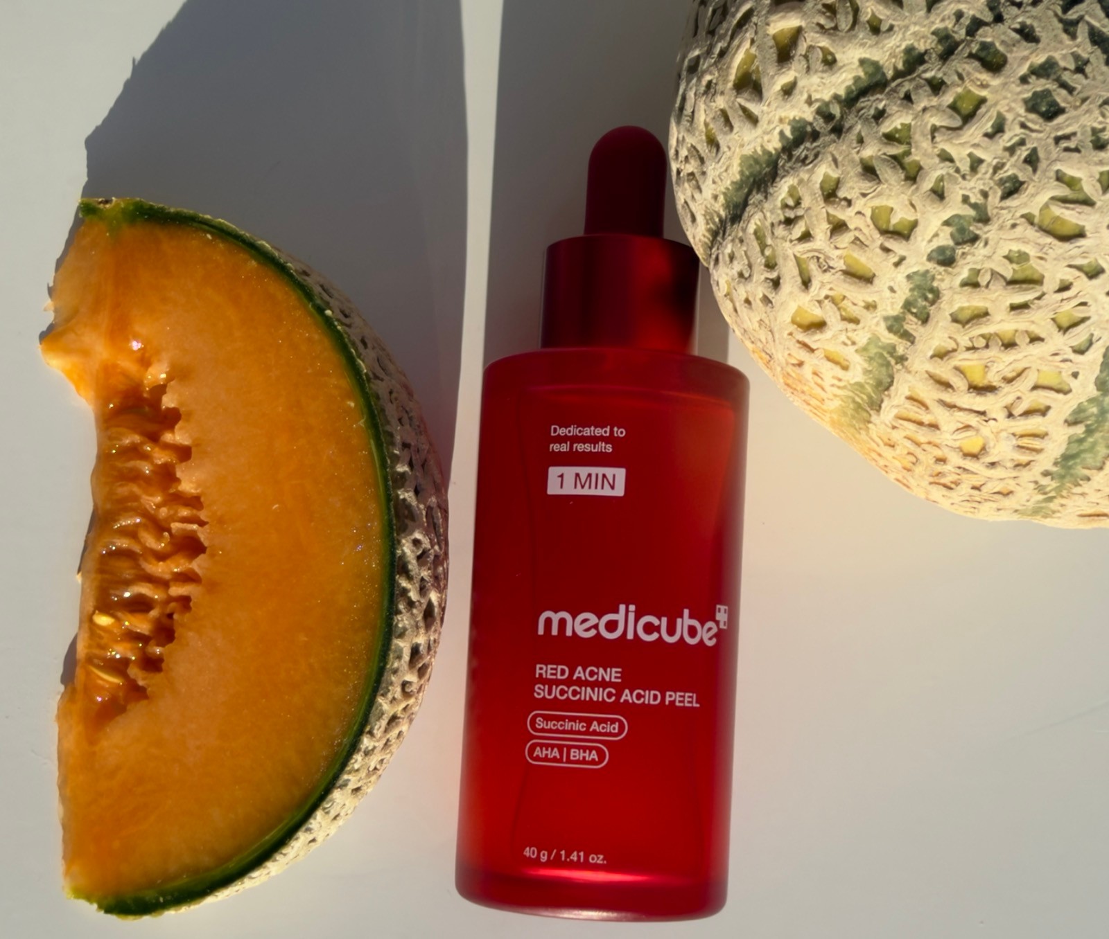 Medicube Red Acne Succinic Acid Peel AHA BHA serum bottle flat lay with cantaloupe melon