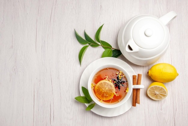 Overview of a herbal tea set-up with white, ceramic tea pot, green tea leaves, cinnamon sticks and lemon