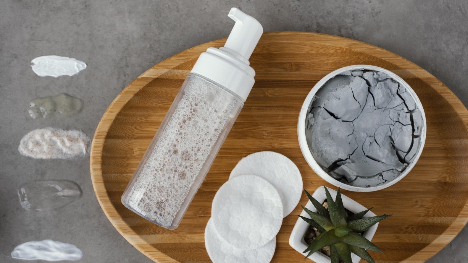 Bubbly face cleanser sitting on wooden tray with clay mask and toner pads