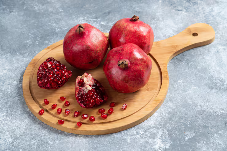 Trio of fresh pomegranates sitting on a wooden paddle board