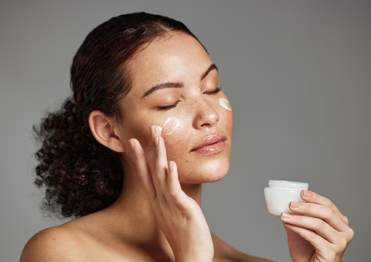Model using face cream on her cheek, her hair tied back
