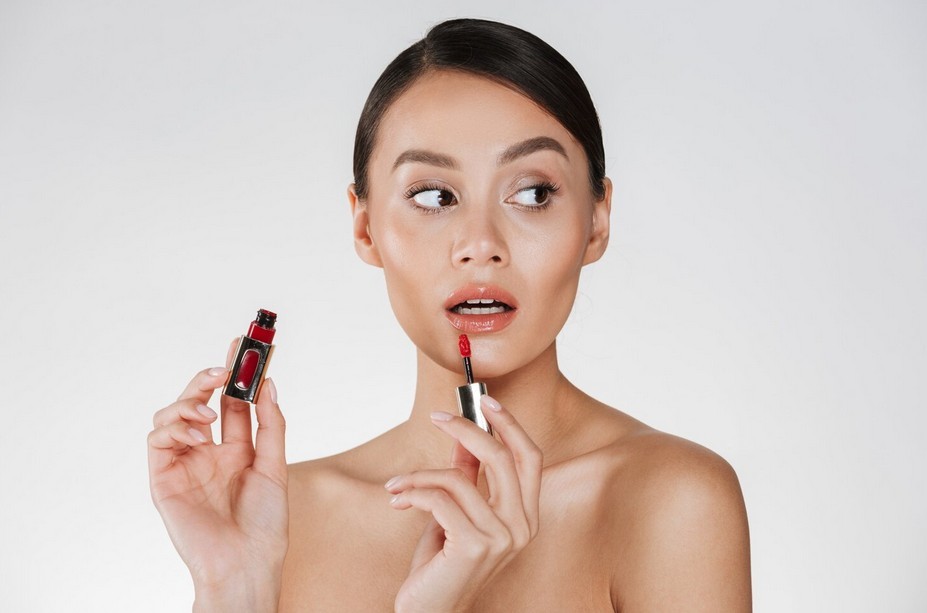 young woman applying lip gloss whilst posing and looking to her left