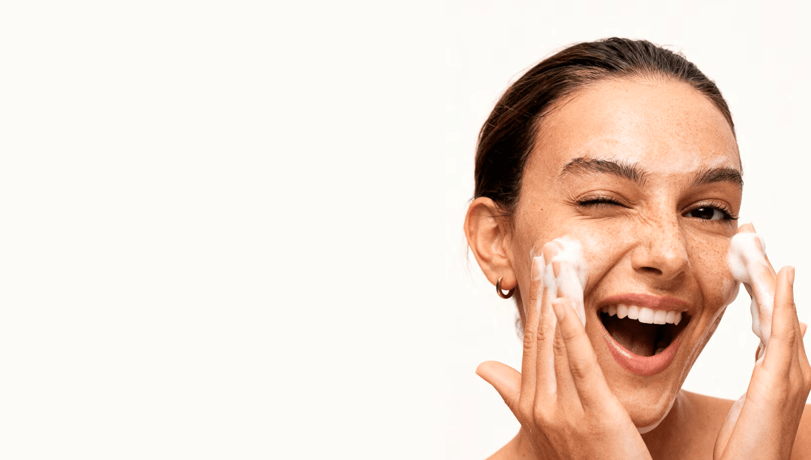 Woman smiling and cleansing her face with a bubbly foam