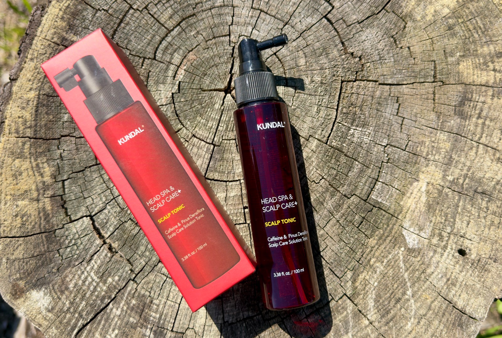 KUNDAL Head Spa & Scalp Care+ Scalp Tonic bottle and red box lying on a rustic wooden tree stump slice