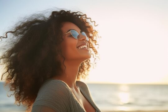 Young woman with sunglasses and black, curly hair smiling at the beach