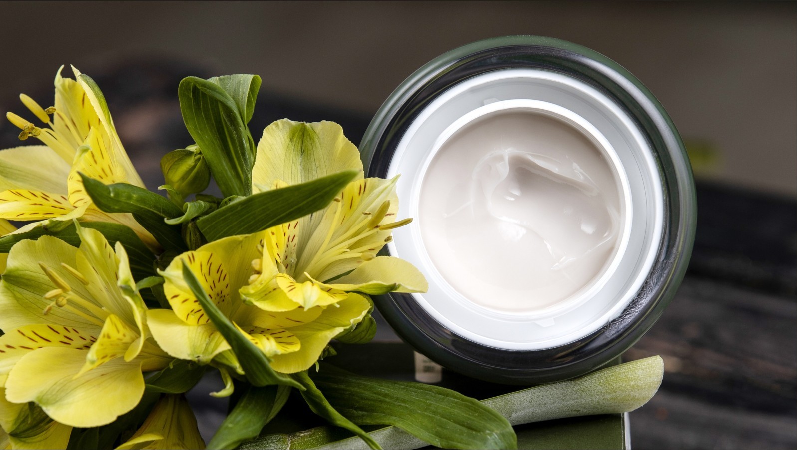 Pot of open moisturizer sitting next to a bright-yellow tiger lily flower