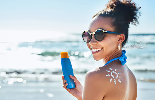 Smiling woman at the beach, applying sunscreen in a sun-shape