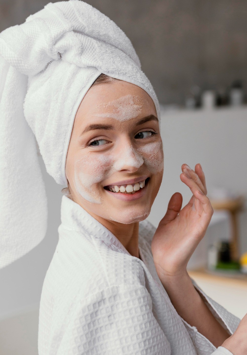 Woman with bubbly foam on her face, smiling in a bathrobe