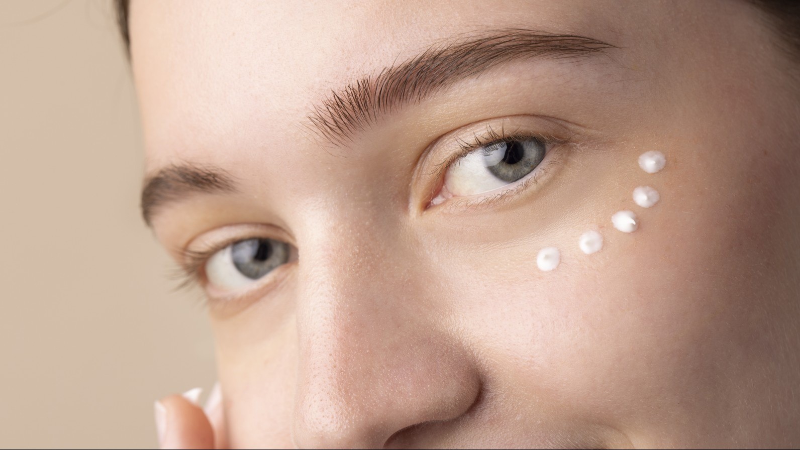 Close up to young woman's face with blue eyes and dots of eye cream under her left eye