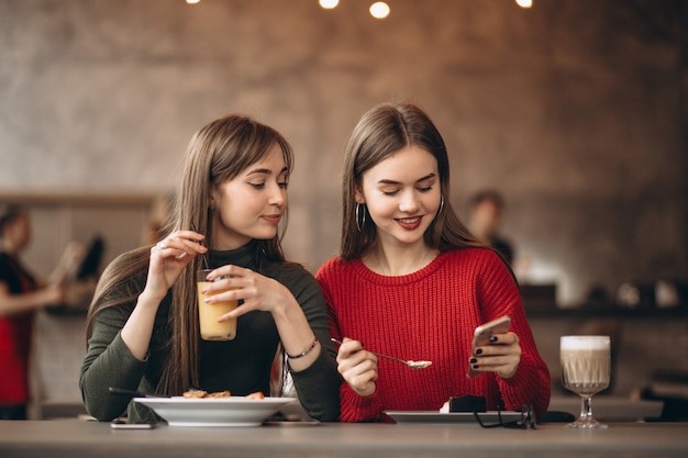 Two women at a cafe looking at a phone together, smiling