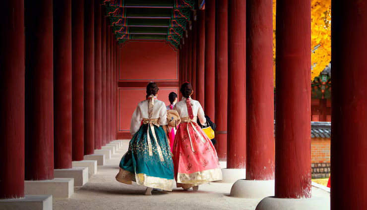 Traditional Korean women dressed in Hanbok, walking through a temple passageway in Autumn.