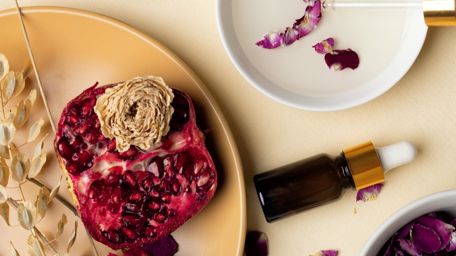 Cracked pomegranate and various potpourri scattered around a serum bottle