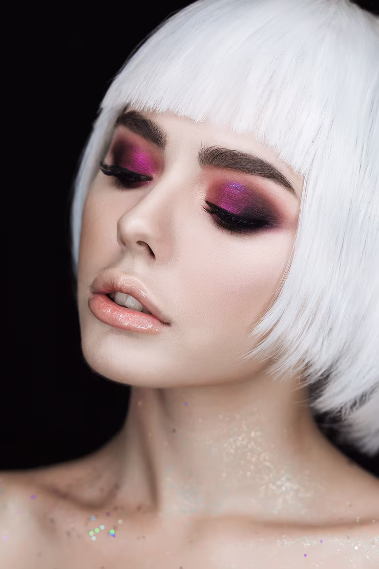 Pale woman posing in dark lighting with purple-glitter eyeshadow and glitter on skin