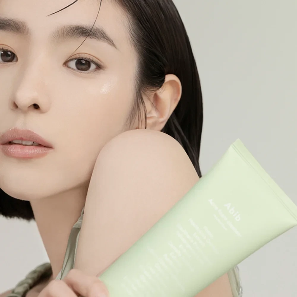 Model holding Abib Acne Foam Cleanser Heartleaf Foam bottle over her shoulder