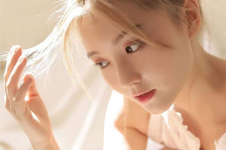 Pale woman sitting in low lighting with sunlight-lit blonde hair