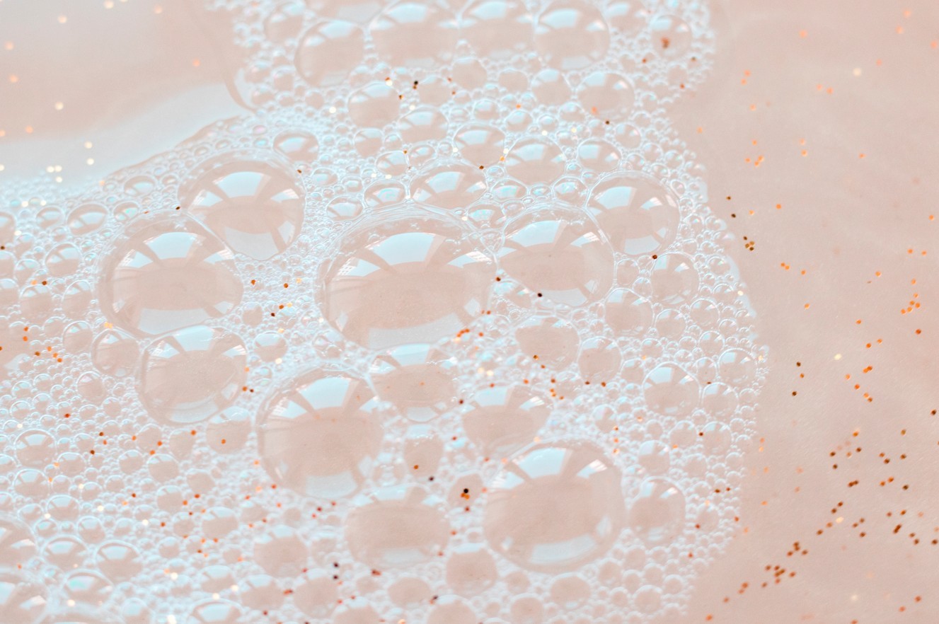 White soapy bubbles on a soft pink, glittery backdrop
