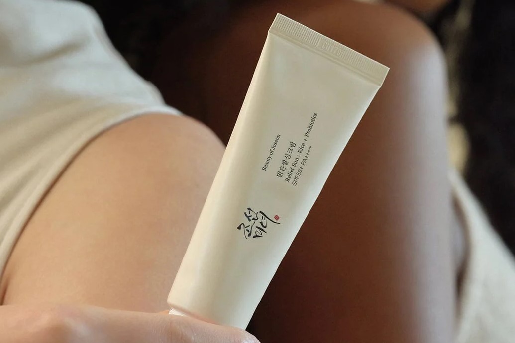 Woman holding Beauty of Joseon Relief Sun: Rice + Probiotics tube in hand with another lady behind her in close up.